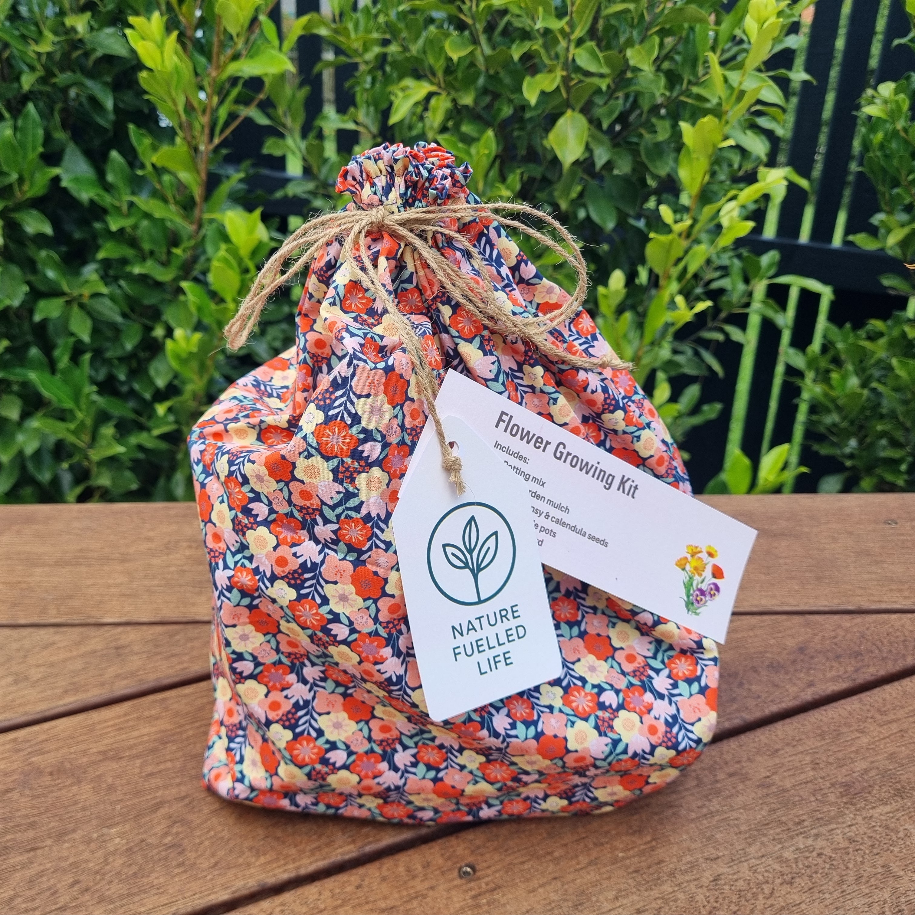 Floral-patterned bag with a tag labeled 'Nature Fueled Life' on a wooden surface with greenery in the background.