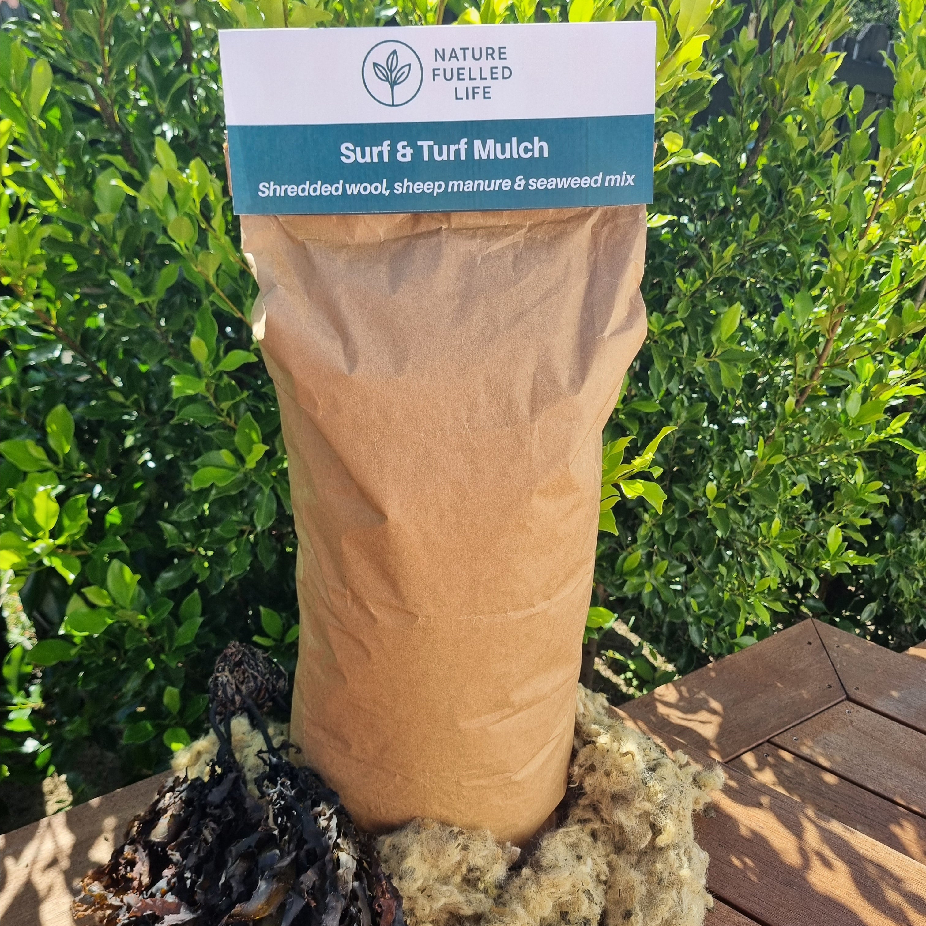 Bag of surf turf mulch with a label on a wooden surface and green foliage background