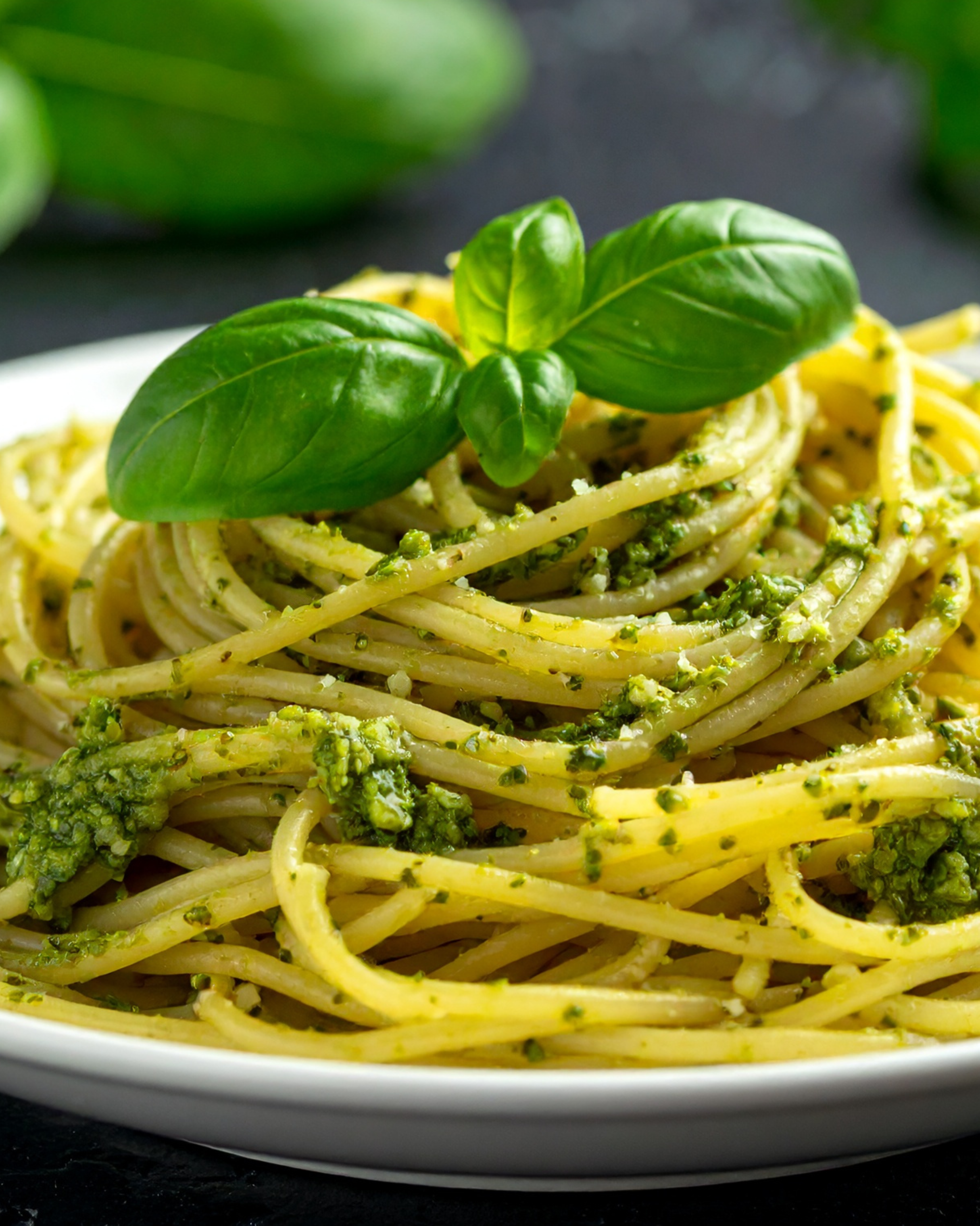 Spaghetti with green pesto sauce and basil leaves on a white plate.